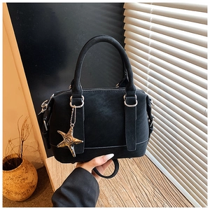 Détail du sac à main noir en daim avec breloque étoile dorée sur une surface en bois