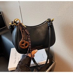 Detail of black crescent shoulder bag with leather texture and creative charms