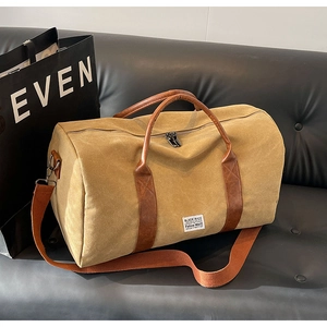 Détail du sac de voyage en toile kaki avec poignées en cuir marron sur canapé noir