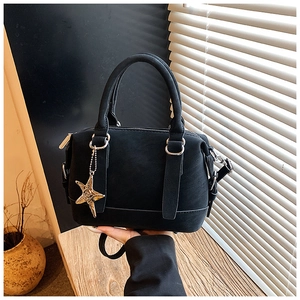 Détail du sac boston noir mat avec un pendentif étoile de mer dorée sous une lumière douce