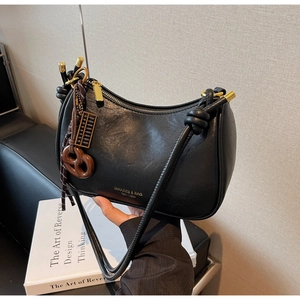 Detail of minimalist black crescent bag with knotted strap and vintage golden pendant