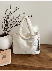 Detailed view of floral embroidery on a white silk tote bag with an elegant jade tassel