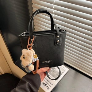 Detail of black matte tote bag with silver studs and cute blue teddy bear pendant