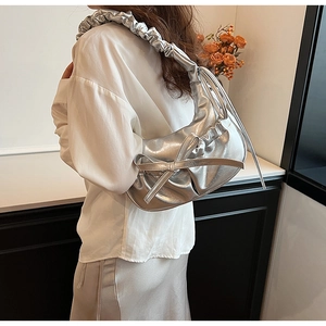 Détail du sac à main argenté métallisé avec nœud et bandoulière plissée sur modèle