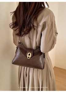 Sophisticated retro dark brown leather bag with a gold oval clasp worn as a shoulder bag