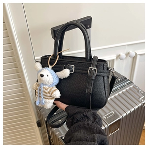 Close-up of black pebble leather bucket bag with silver hardware and a cute teddy bear charm