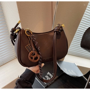 Detail of dark brown leather crescent bag with decorative knot and pretzel charm