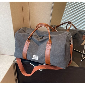 Détail du sac de voyage en toile grise montrant les poignées en cuir brun et la bandoulière