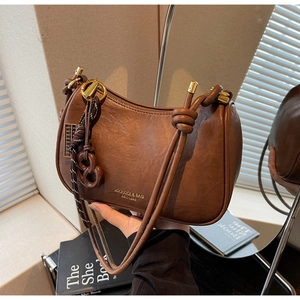 Detail of a brown leather crescent shoulder bag with golden zipper and braided rope decor