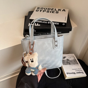 Detail view of light blue leather bucket bag with brand logo and cute bear charm