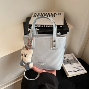 Detail of light blue PU leather bucket bag featuring a cute teddy bear charm and strap