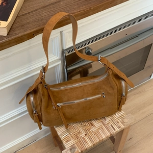 Detail of tan suede Boston bag with silver zippers and adjustable strap on a stool