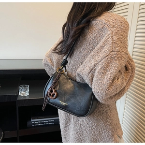Detail of black faux leather half-moon bag featuring gold logo and brown braided charm