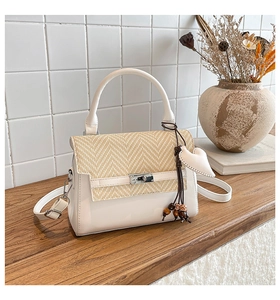 Detail of white crossbody bag with woven wave pattern flap and heart pendant charm