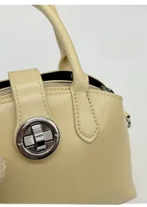 Close-up of a cream leather handbag featuring a silver circular metal clasp and fine stitching