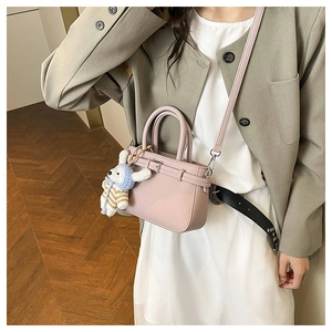 Pink lychee leather bucket bag with cute bunny pendant shown on a model in olive blazer
