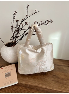 Close-up of champagne satin tote bag with floral embroidery and elegant jade tassel charm