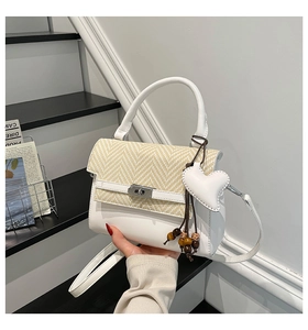 Detail of white leather handbag featuring woven straw lid and heart-shaped leather charm