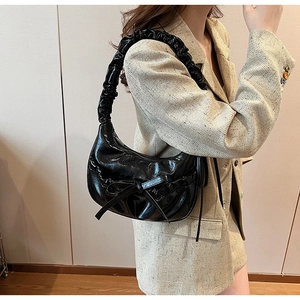 Détail du sac à nœud noir brillant avec anse plissée et forme demi-lune sur modèle