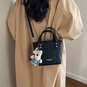 Close-up of black leather bucket bag with top handle and cute white teddy bear charm