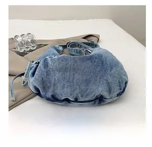 Detailed close-up of blue denim crescent bag showing washed texture and drawstring design