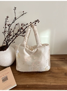 Detail of elegant champagne satin tote bag with floral embroidery and bead tassel charm