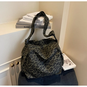 Detailed view of leopard print tote bag with black wide strap on a soft fabric stool