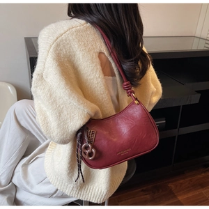Detail of dark red leather shoulder bag with gold logo and stylish knotted strap design
