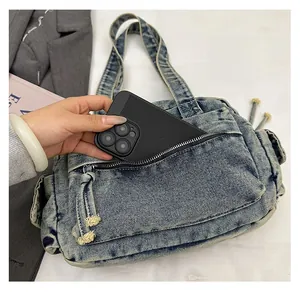 Detail of light blue denim tote bag showing a large front zipper pocket for smartphone storage