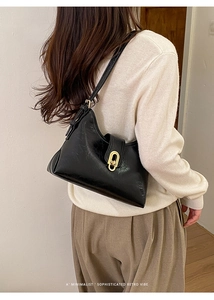 Side view of black glossy leather underarm bag featuring a gold oval metallic buckle