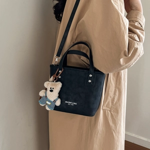Detail of matte black tote bag with brand lettering and blue denim bear charm
