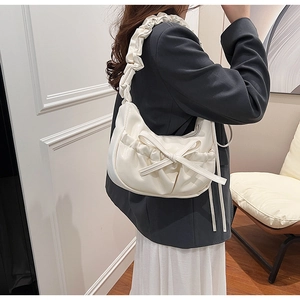 Détail du sac croissant crème avec nœud et anse froncée sur un blazer gris