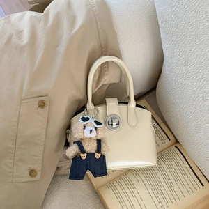 Detail of beige leather handbag with cute teddy bear charm and silver twist lock closure