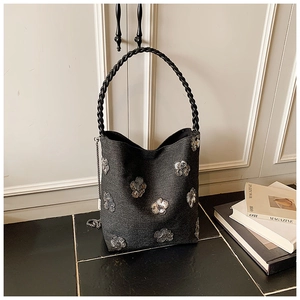 Detail of black bucket bag with silver sequin flowers and a braided handle on the floor