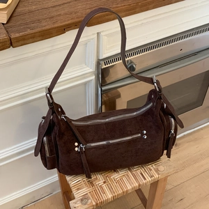 Close-up of dark brown suede hobo bag with decorative silver zippers and rivets