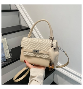 Close-up of cream crossbody bag featuring woven texture flap and heart pendant detail