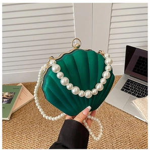 Detail of emerald shell-shaped acrylic clutch bag with pearl handle and metal chain strap