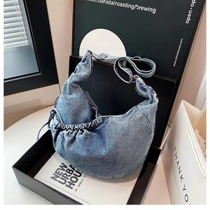 Detail of blue denim hobo bag featuring pleated bottom texture and adjustable strap