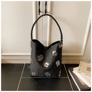 Detail of black denim shoulder bag with silver sequin floral patterns and woven strap