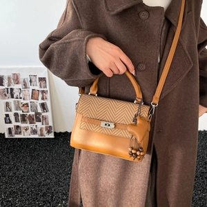 Detailed close-up of brown crossbody bag featuring herringbone fabric and heart charm