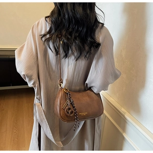 Close-up of brown leather underarm bag with gold logo and woven knot keychain detail