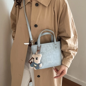 Close-up of a light blue mini tote bag with a cute bear charm and a thin shoulder strap