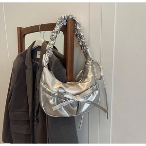 Détail du sac hobo argenté avec nœud papillon et anse plissée sur une chaise en bois