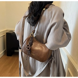 Detail of a brown leather hobo bag featuring a knotted shoulder strap and gold brand logo