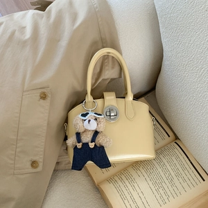 Detail of yellow vintage handbag with silver lock and a teddy bear charm on open books