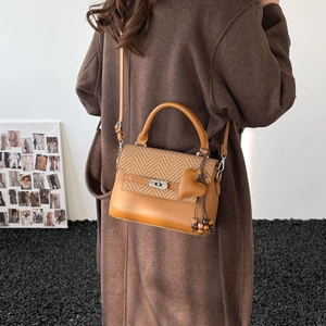Detail of tan leather crossbody bag with herringbone weave and heart pendant on a model