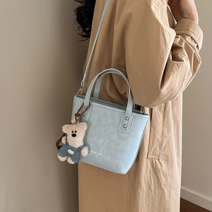 Light blue textured tote bag detail featuring a plush bear charm and rivet handle