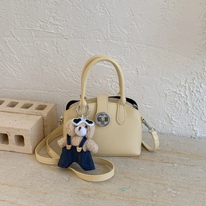 Detail of beige leather handbag featuring a round metal clasp and cute teddy bear charm