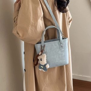 Detail of light blue leather bucket bag with rivet decor and cute plush bear charm
