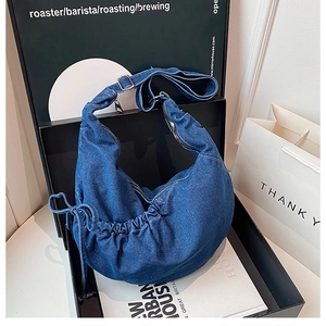 Detail of blue denim hobo bag with adjustable strap and metal hardware in a display box